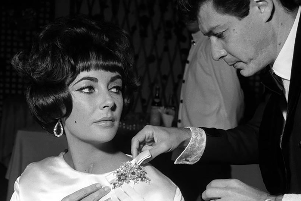 Elizabeth Taylor with Eddie Fisher who is adjusting her Bulgari emerald and diamond flower brooch